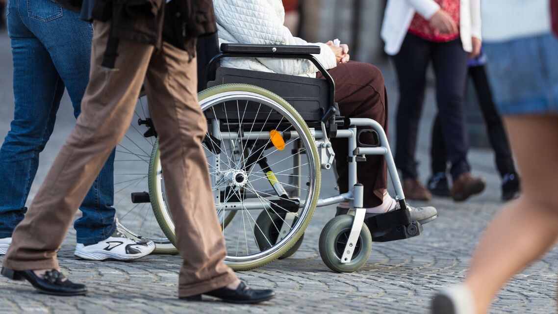 a lady in a wheelchair outside with out people walking around. waist down view