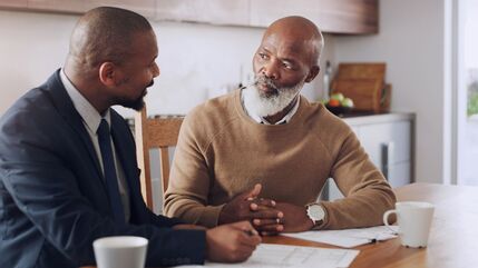 2 men sit at a desk, 1 man advising the other, older man