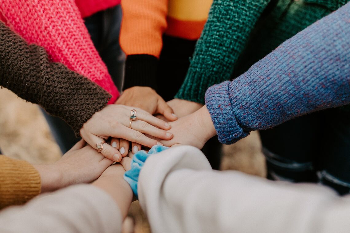 Multiple people in a circle with only their arms visible, up to the elbow, with their hands touching in the middle