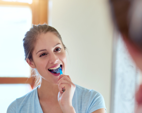woman brushing her teeth in the mirror