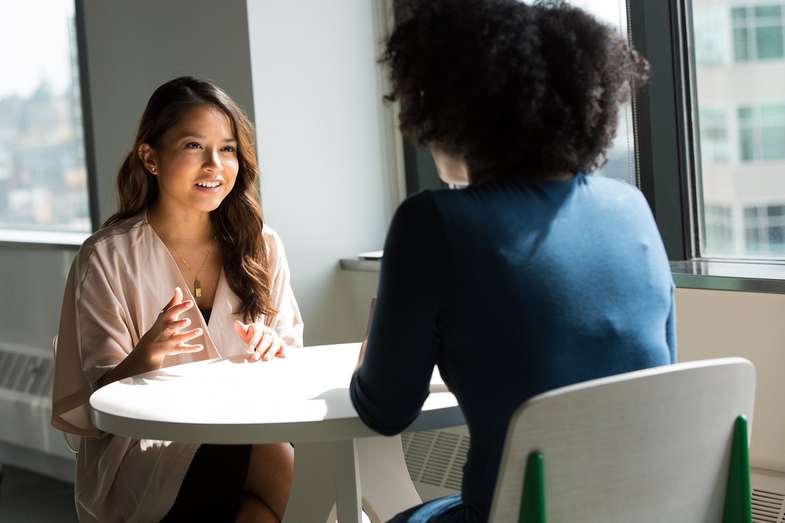 Two women sitting down at a table facing each other and having a conversation