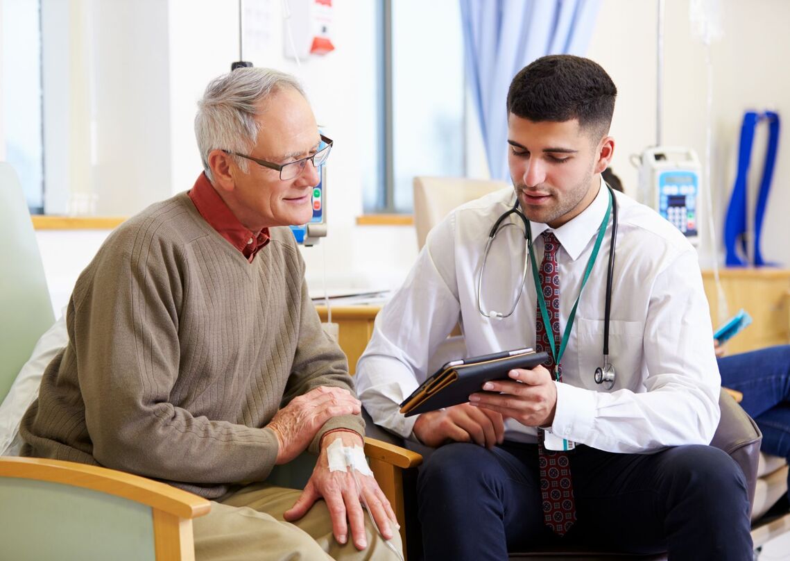 Older man sits with a doctor, they both consult an ipad 