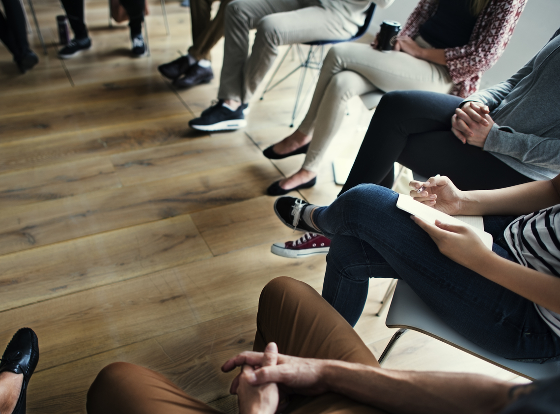 View of people's feet and lower body as they sit in a semi-circle listening to a workshop