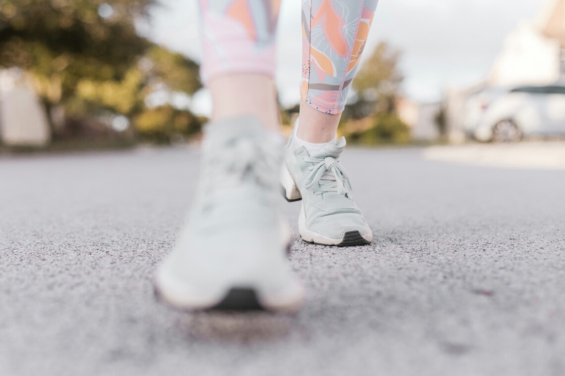 A close up of a woman's feet in white trainers walking down a road with a blurry background