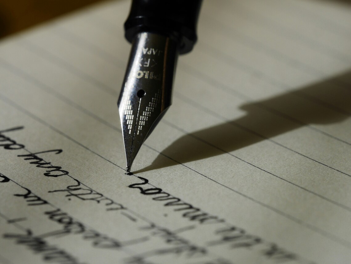 A fountain pen writing on a page in ink; one half of the page already has writing and one half is blank