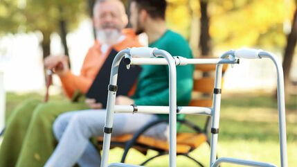 old man and younger man sitting on a park bench in background with walking frame in foreground