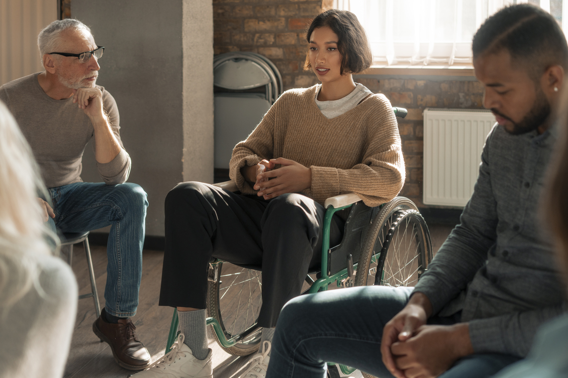 A woman in a wheelchair is in circle talking while a group of people listen