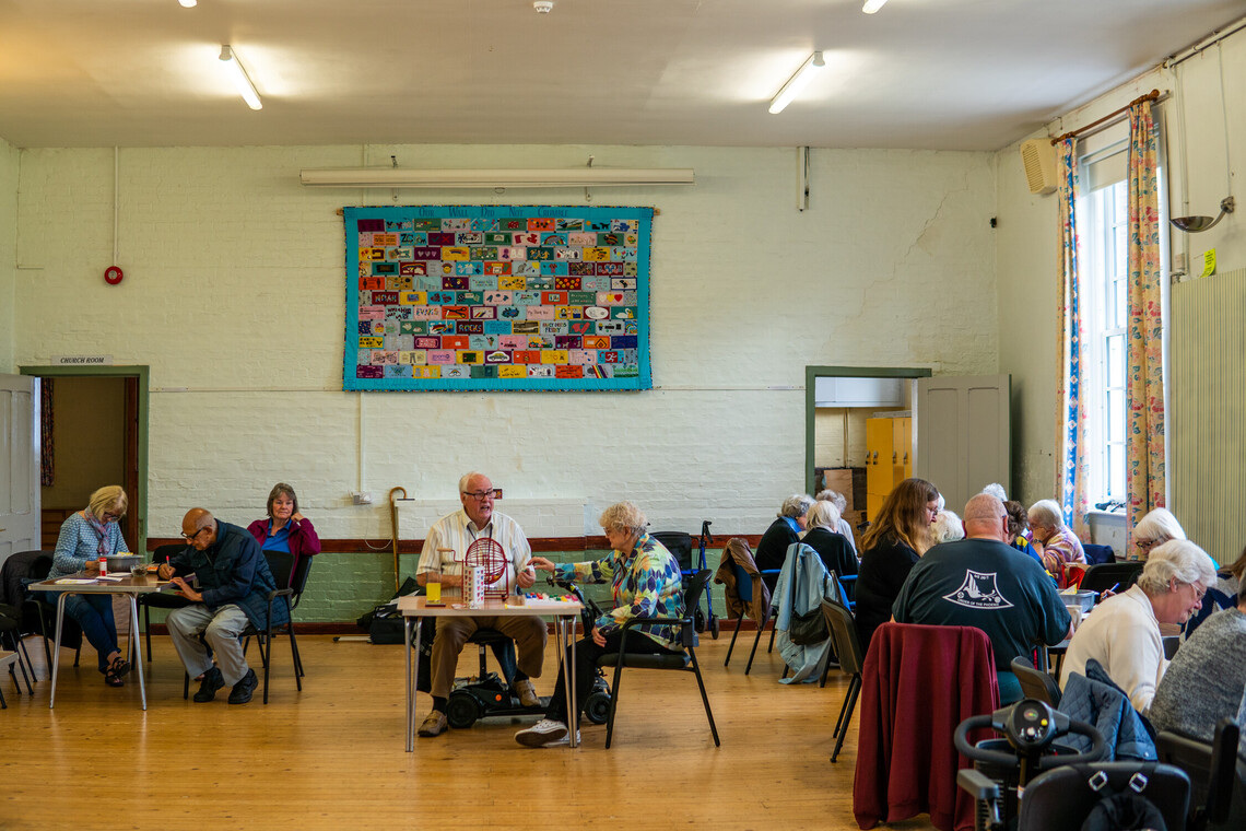 Group of older people doing activities at tables in community hall