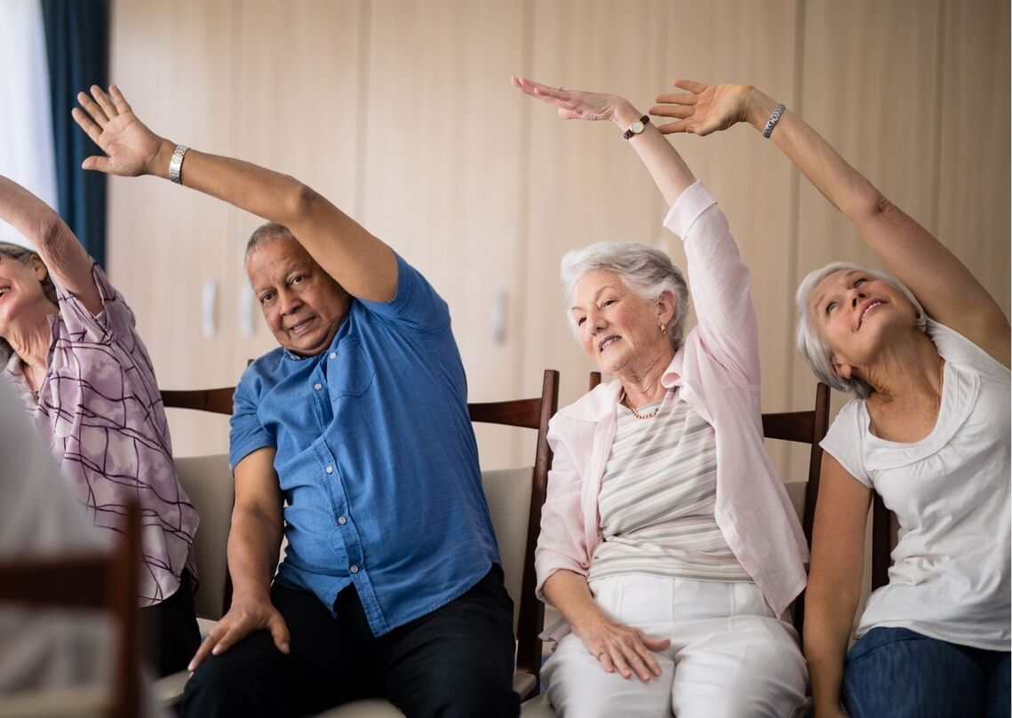 Group of 4 older people doing overhead stretches whilst seated on chairs 
