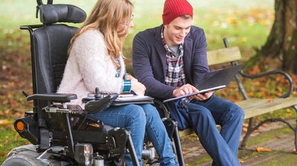 man sits on a park bench next to a woman in a wheelchair