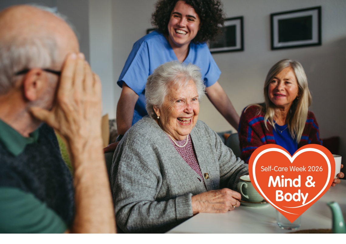3 older people sat down laughing with a carer stood with them