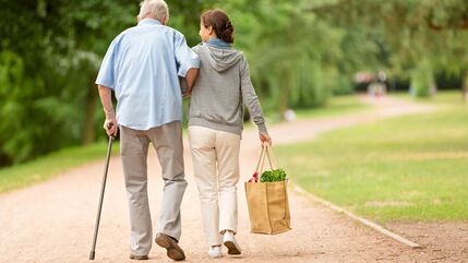 woman helping older man with shopping bags as they walk along a path