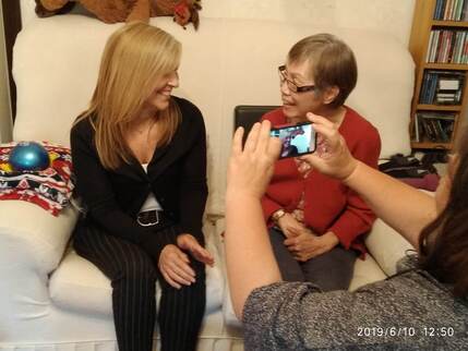 2 women sat chatting happily on a sofa whilst being filmed for a volunteer video. Film making back to the camera