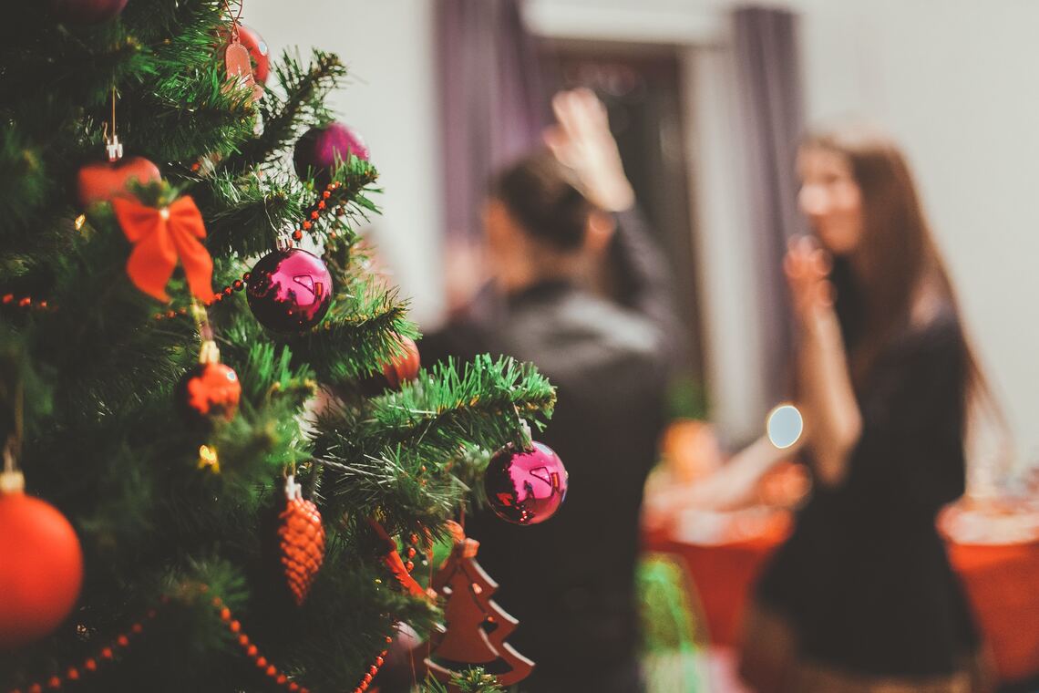 A decorated Christmas tree on the left-hand side with blurred people in the background on the right-hand side dancing and talking