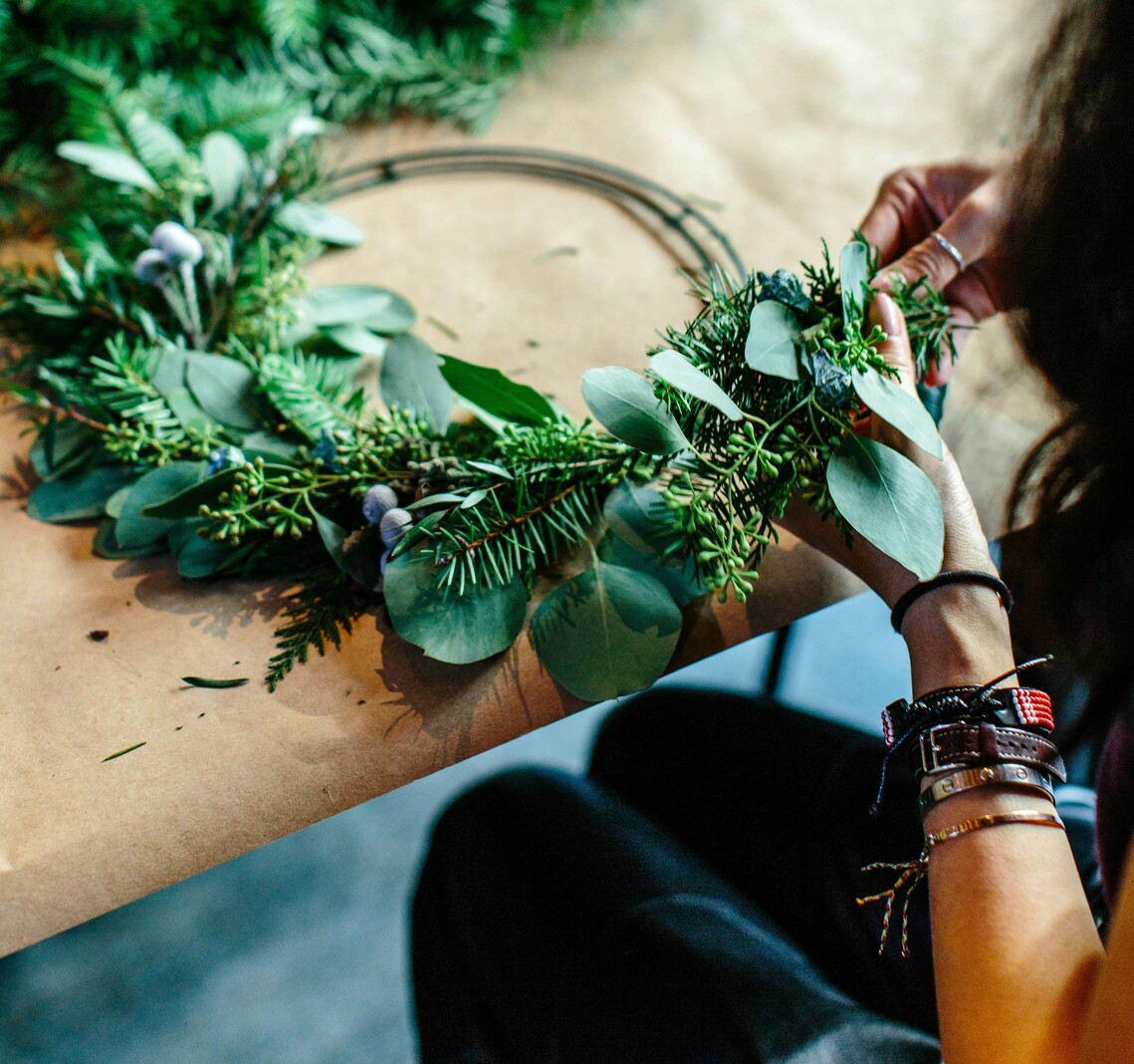 A woman in the process of making a Christmas Wreath with spruce and leaves sitting at a table