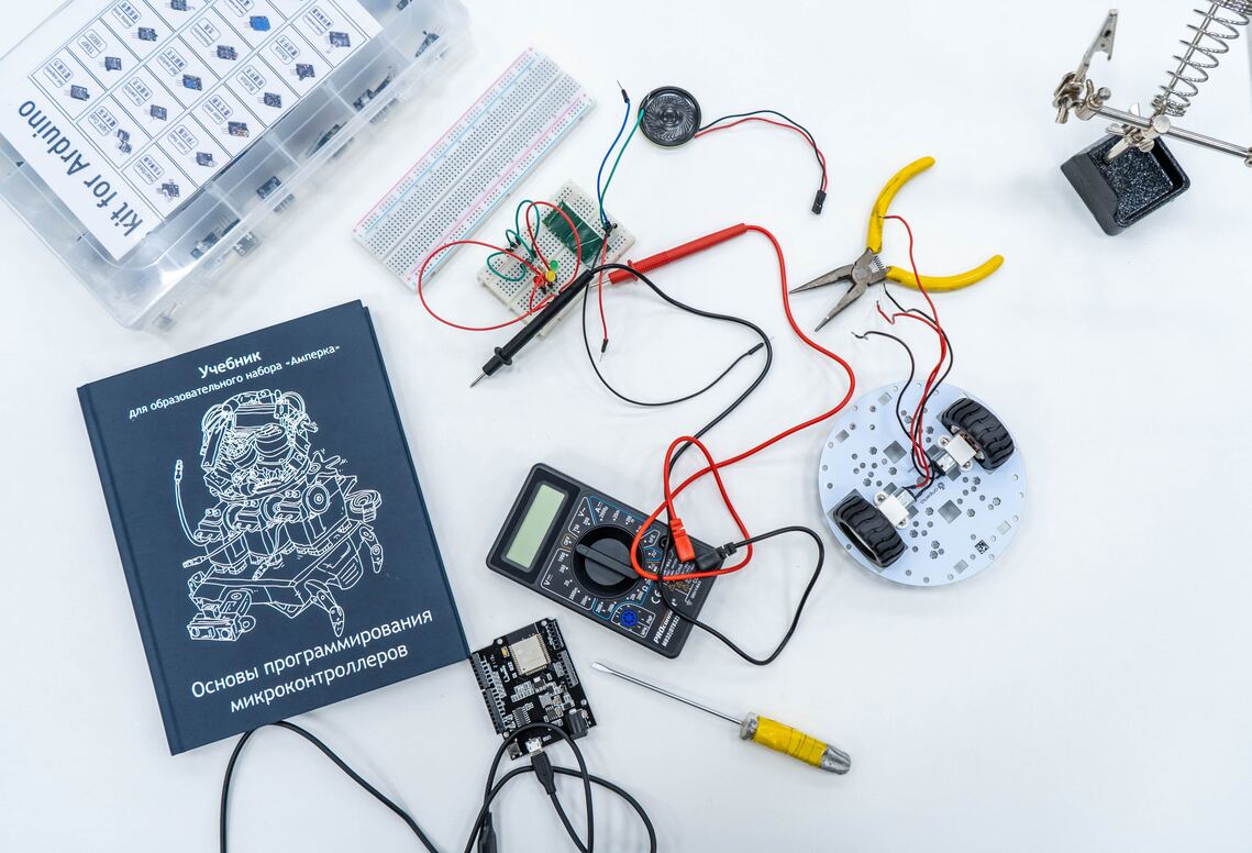 Miscellaneous items associated with building a robot strewn around a desk including wires, pliers, a screedriver, a robot kit etc.