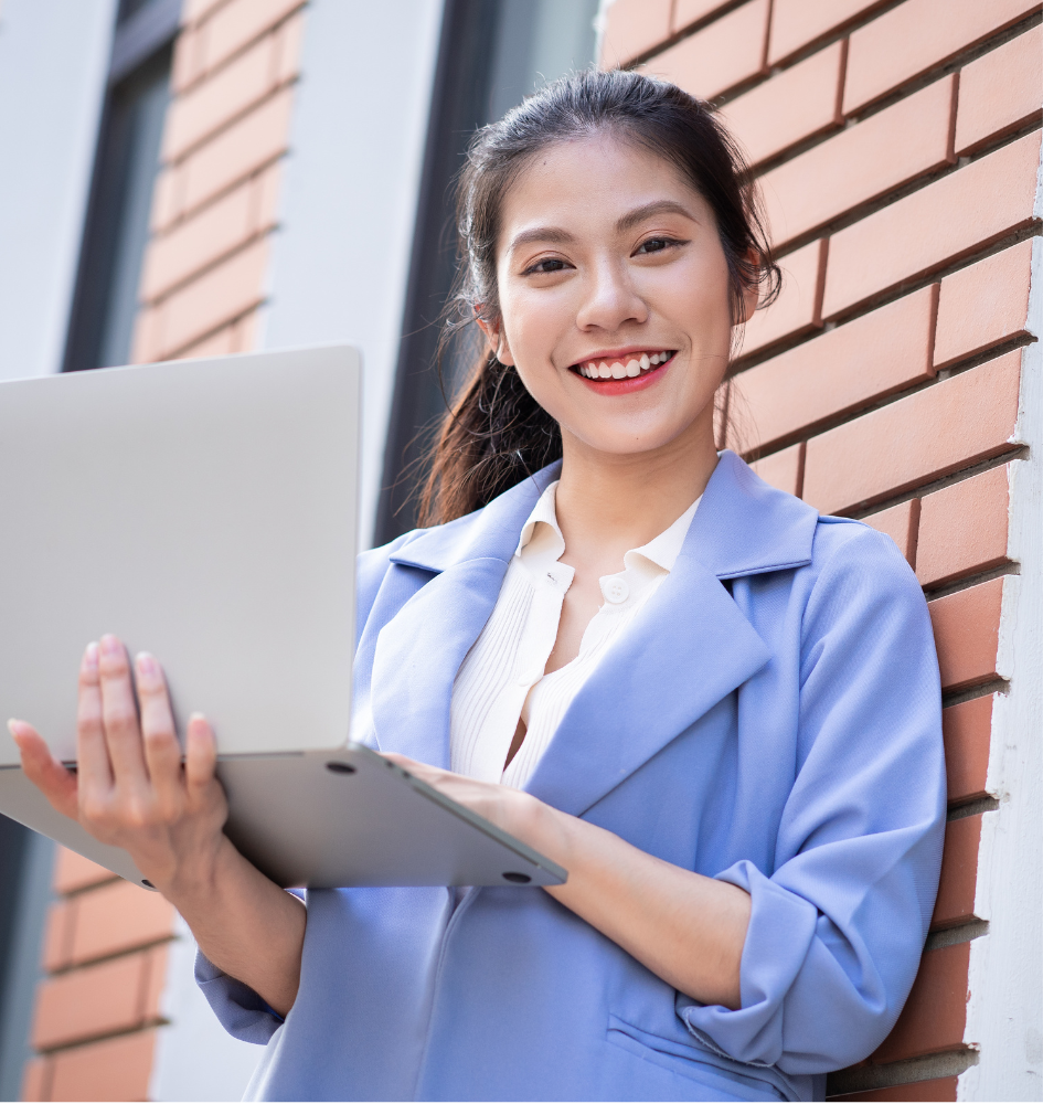 young woman standing holding an open laptop, smiling at camera